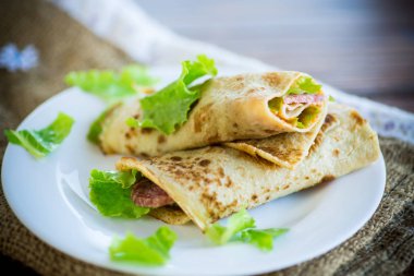 salata yaprakları ve ahşap bir masa üzerinde bir tabak içinde pastırma ile ince krep