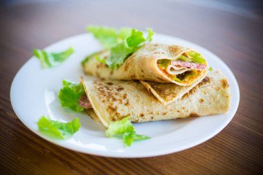 salata yaprakları ve ahşap bir masa üzerinde bir tabak içinde pastırma ile ince krep