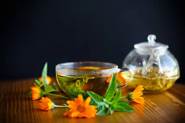 在木桌上的玻璃杯里用香草和万寿菊花的新鲜热茶 — 图库照片