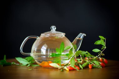 Olgun kırmızı goji meyveleri siyah bir arka plan üzerinde izole bir cam çaydanlık sıcak çay