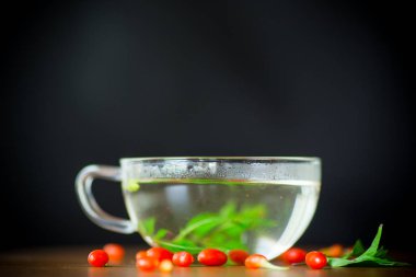 Olgun kırmızı goji meyveleri siyah bir arka plan üzerinde izole bir cam çaydanlık sıcak çay