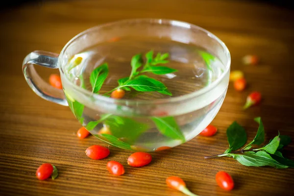 Olgun kırmızı goji meyveleri ahşap bir masa üzerinde bir cam çaydanlık sıcak çay