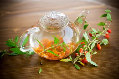 Olgun kırmızı goji meyveleri ahşap bir masa üzerinde bir cam çaydanlık sıcak çay