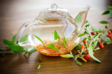 Olgun kırmızı goji meyveleri ahşap bir masa üzerinde bir cam çaydanlık sıcak çay