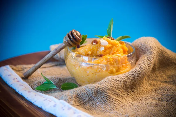 boiled sweet pumpkin porridge with raisins and nuts in a glass bowl on a blue background