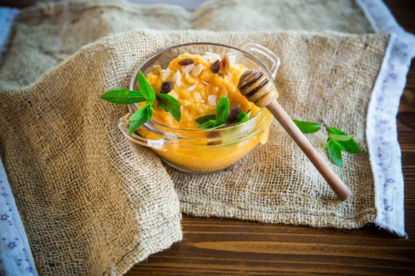 boiled sweet pumpkin porridge with raisins and nuts in a glass bowl on wooden background