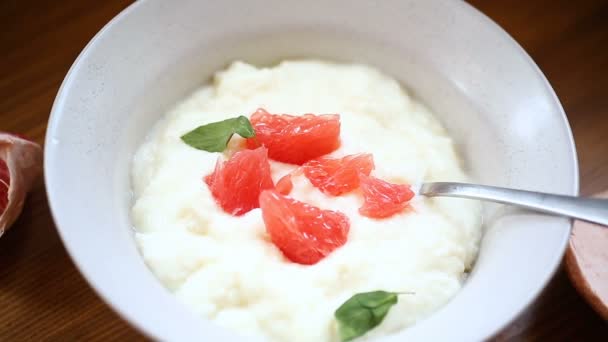 Avena de sémola hervida dulce en un plato con rodajas de pomelo rojo — Vídeo de stock