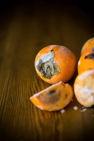 木製の背景に氷で熟した柿を冷凍 — ストック写真