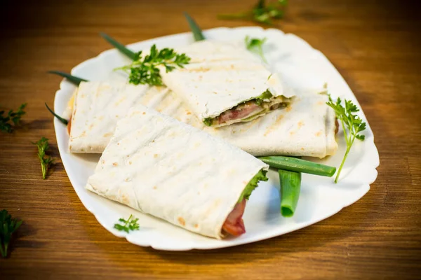 Rollo de pita con hojas de lechuga, verduras y salchichas en un plato — Foto de Stock