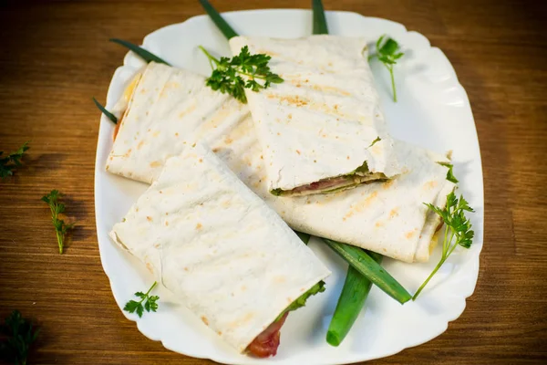 Rollo de pita con hojas de lechuga, verduras y salchichas en un plato — Foto de Stock