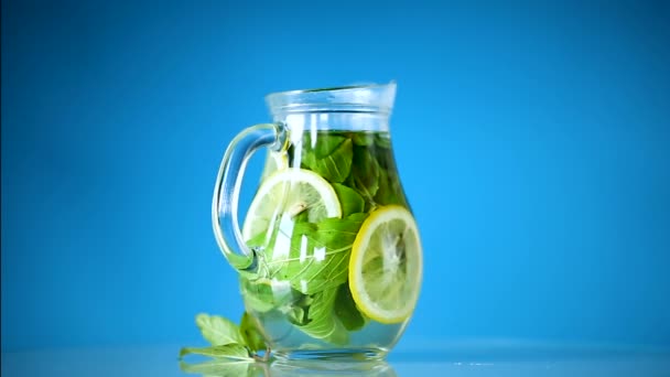 Citronnade fraîche froide aux citrons et menthe dans une carafe isolée sur bleu — Video