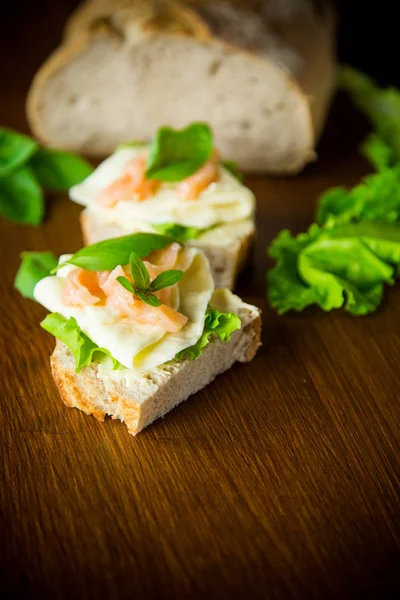 Sandwich mit Käse, Salatblättern und rotem Fisch auf einem Holztisch — Stockfoto