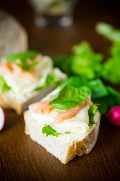 Sandwich mit Käse, Salatblättern und rotem Fisch auf einem Holztisch — Stockfoto