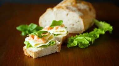 peynir, salata yaprakları ve ahşap üzerinde kırmızı balık ile sandviç