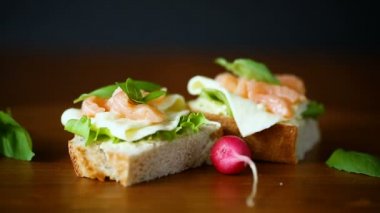 peynir, salata yaprakları ve ahşap üzerinde kırmızı balık ile sandviç