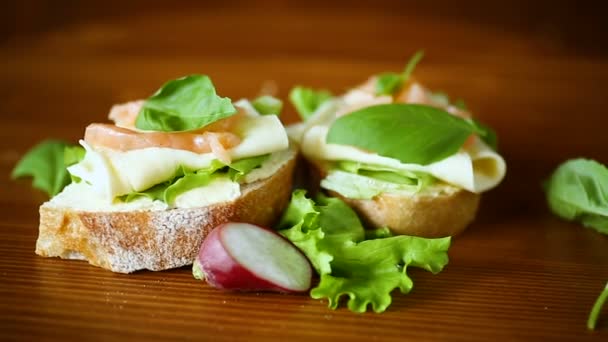 Sandwich met kaas, salade blaadjes en rode vis op een houten — Stockvideo