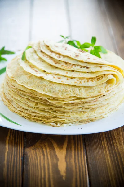 Veel gebakken dunne pannenkoeken in een bord, op een tafel. — Stockfoto