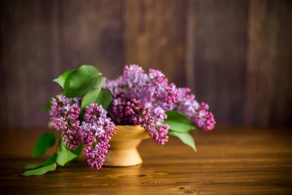 bouquet of beautiful blooming lilacs in a vase on a wooden table
