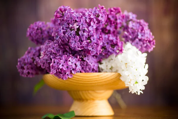 木制桌子上的木制花瓶里有一束漂亮的紫色紫丁香 — 图库照片