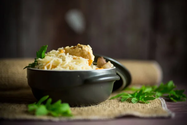 Варёный рис с овощами и мясом в керамической миске на деревянном столе — стоковое фото