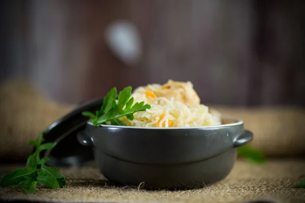 Варёный рис с овощами и мясом в керамической миске на деревянном столе — стоковое фото