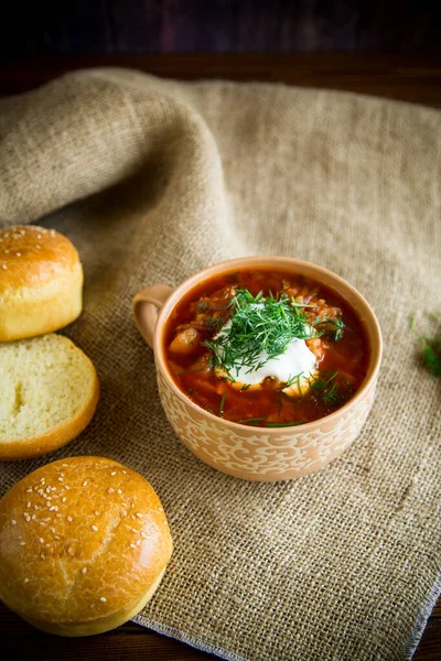 Гарячий буряковий суп зі сметаною, травами та рулетами в керамічній мисці — стокове фото