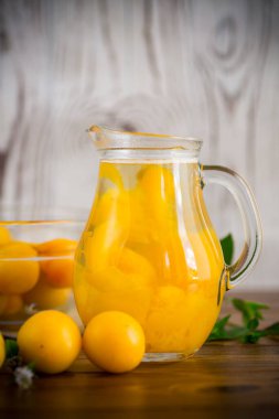 Tahta bir masada, olgun sarı kiraz eriğinde cam bir sürahide pişirilmiş komposto.