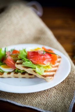 Salata yapraklı kızarmış ekmek ve ahşap bir masada tuzlanmış kırmızı balık.