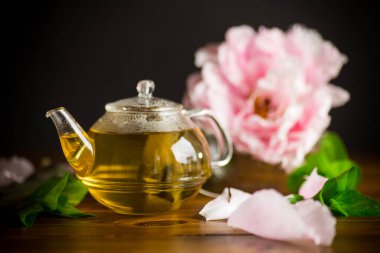 Tahta bir masada, cam çaydanlıkta gül yapraklarından gelen yaz çiçeği çayı.