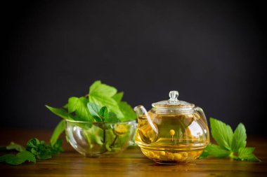 Yaz mevsiminin ferahlatıcı organik çayı, ahşap bir masanın üzerindeki cam çaydanlıkta üzümlü yapraklardan elde edilir.