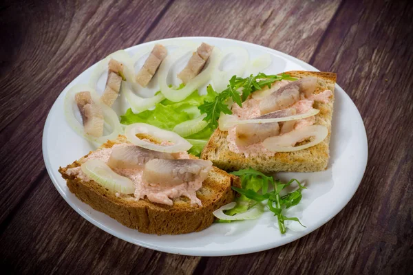 テーブルの上の皿にサラダとニシンと玉ねぎとハーブのサンドイッチ — ストック写真