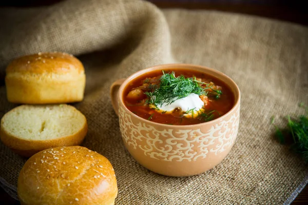 Sopa de remolacha caliente con crema agria, hierbas y rollos en un tazón de cerámica — Foto de Stock