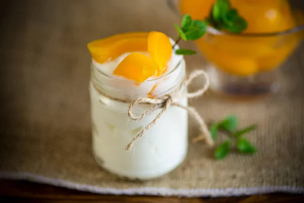 Házi készítésű édes joghurt pácolt őszibarackszeletekkel üvegedényben Stock Fotó