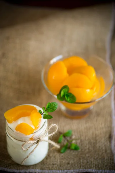 Домашний сладкий йогурт с ломтиками маринованных персиков в стеклянной банке — стоковое фото