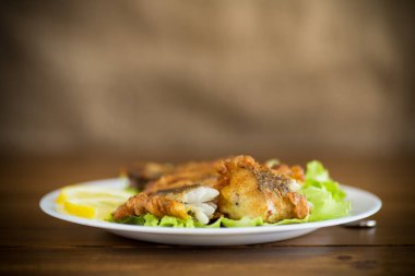 Tahta bir masada, marul ve limonlu hake balığı.