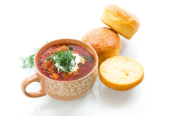 hot beetroot soup with sour cream, herbs and rolls in a ceramic bowl isolated on white background