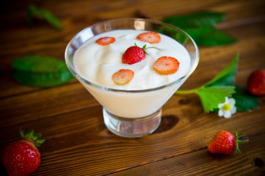 Tahta bir masada cam bir kasede kırmızı taze çilekli ev yapımı yoğurt.