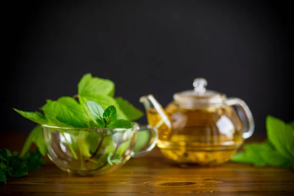 在木制桌子上的玻璃杯茶壶中 用醋栗叶作清凉的绿茶 — 图库照片