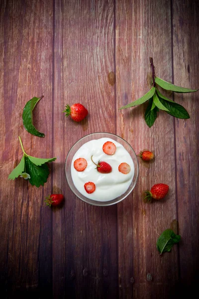 甜的自制酸奶 用红熟的新鲜草莓放在木制桌子上的玻璃碗里 图库图片