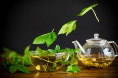 Yaz mevsiminin ferahlatıcı organik çayı, ahşap bir masanın üzerindeki cam çaydanlıkta üzümlü yapraklardan elde edilir.