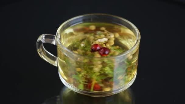 Gorąca herbata ziołowa z różnych ziół w szklanym kubku na czarnym tle — Wideo stockowe