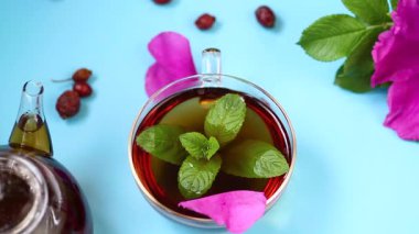 Mavi arka planda gül ağacı, taç yaprağı ve nane yeşili çay servisi.