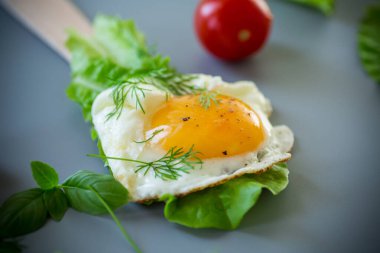 İştah açıcı sahanda yumurta, ahşap spatulada yeşiller, gri arka planda..