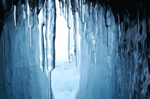 view from  ice cave. frozen, crystal clear water drops like stalactites hang from the ceiling. rising sun stained ice. partially tinted photo. focus on a central object. Extra shallow depth of field.