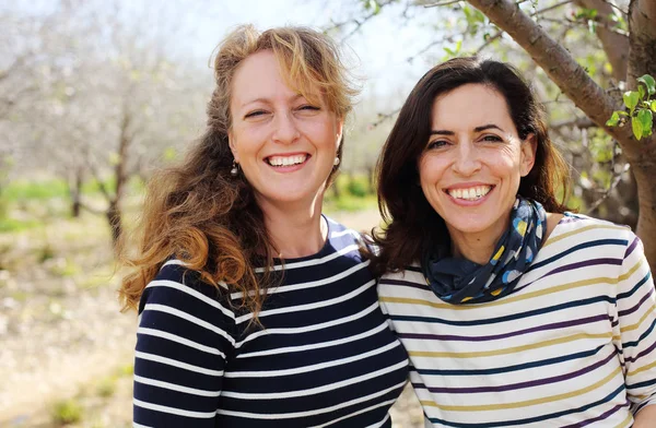 Açık havada gülümseyen iki olgun kadının portresi.