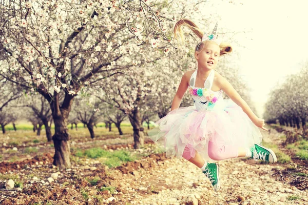 Girl in a unicorn costume jumps outdoors. Spring is around, appl — Stock Photo, Image