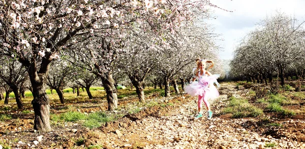 Girl in a unicorn costume jumps outdoors. Spring is around, appl — Stock Photo, Image