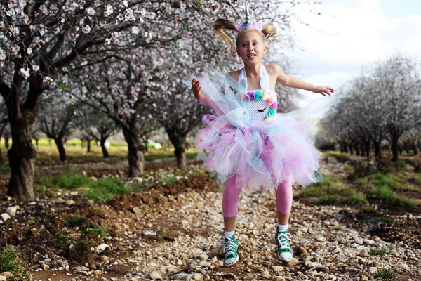 Girl in a unicorn costume jumps outdoors. Spring is around, appl — Stock Photo, Image