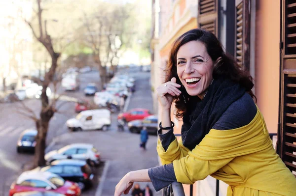 Mooie rijpe vrouw staande op het balkon uitkijken op de st — Stockfoto