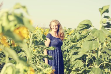 Uzun saçlı mutlu olgun bir kadının portresi. Ayçiçeği tarlasında özgürlüğün tadını çıkarıyor.